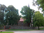 Dorfkirche in Plöwen hinter Bäumen mit Kirchenmauer